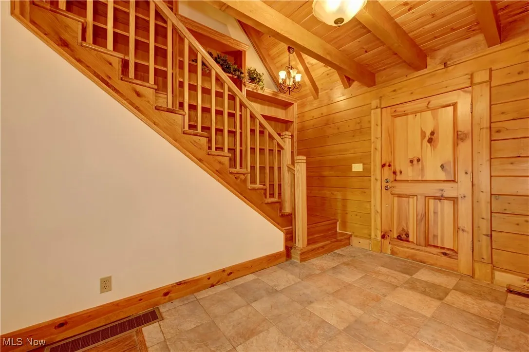 Foyer featuring wooden ceiling, a chandelier, stairs, and wooden walls