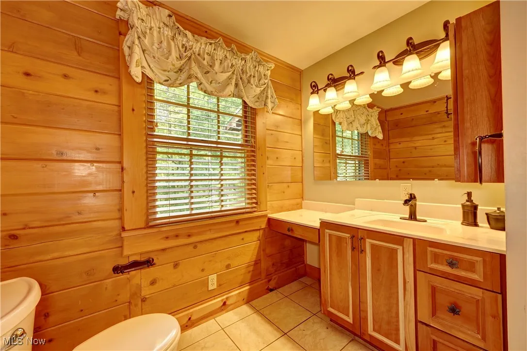 Bathroom with healthy amount of natural light, vanity, tile patterned flooring, and wood walls