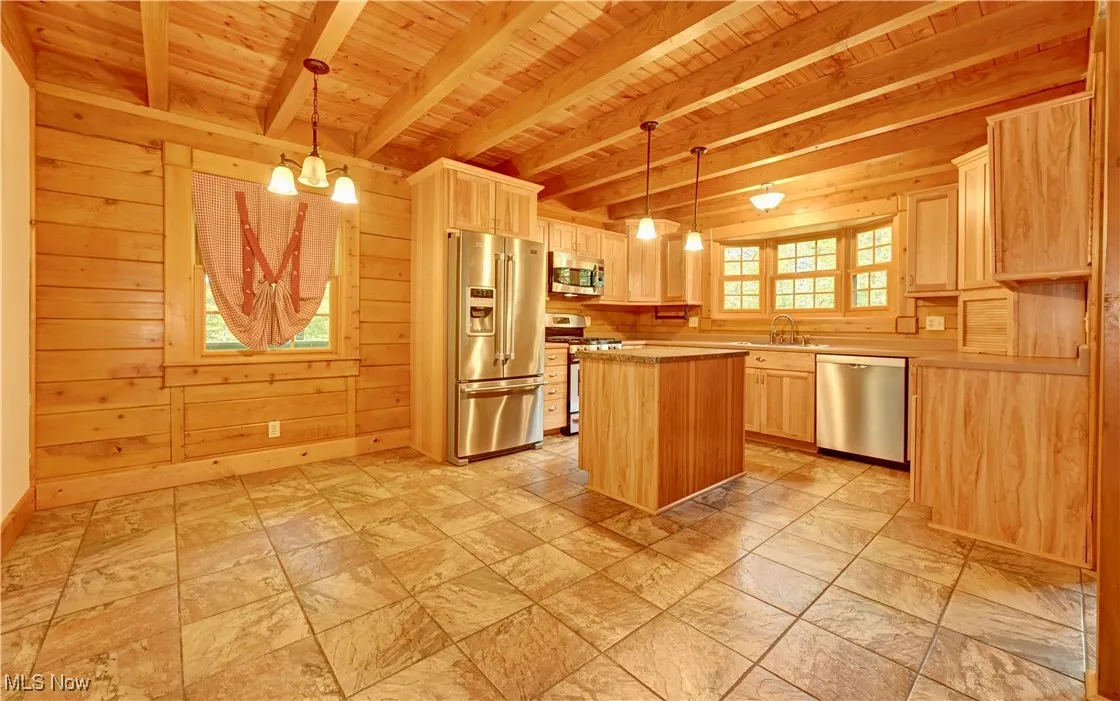 Kitchen featuring stainless steel appliances, light brown cabinetry, a wood ceiling with exposed beams, wood walls, and a chandelier