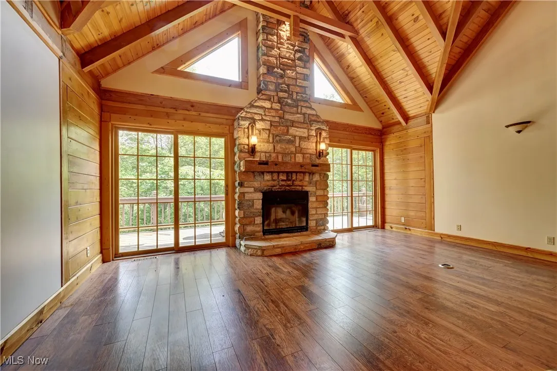 Unfurnished living room with a wooden ceiling with exposed beams, a stone fireplace, wood-type flooring, wooden walls, and high vaulted ceiling
