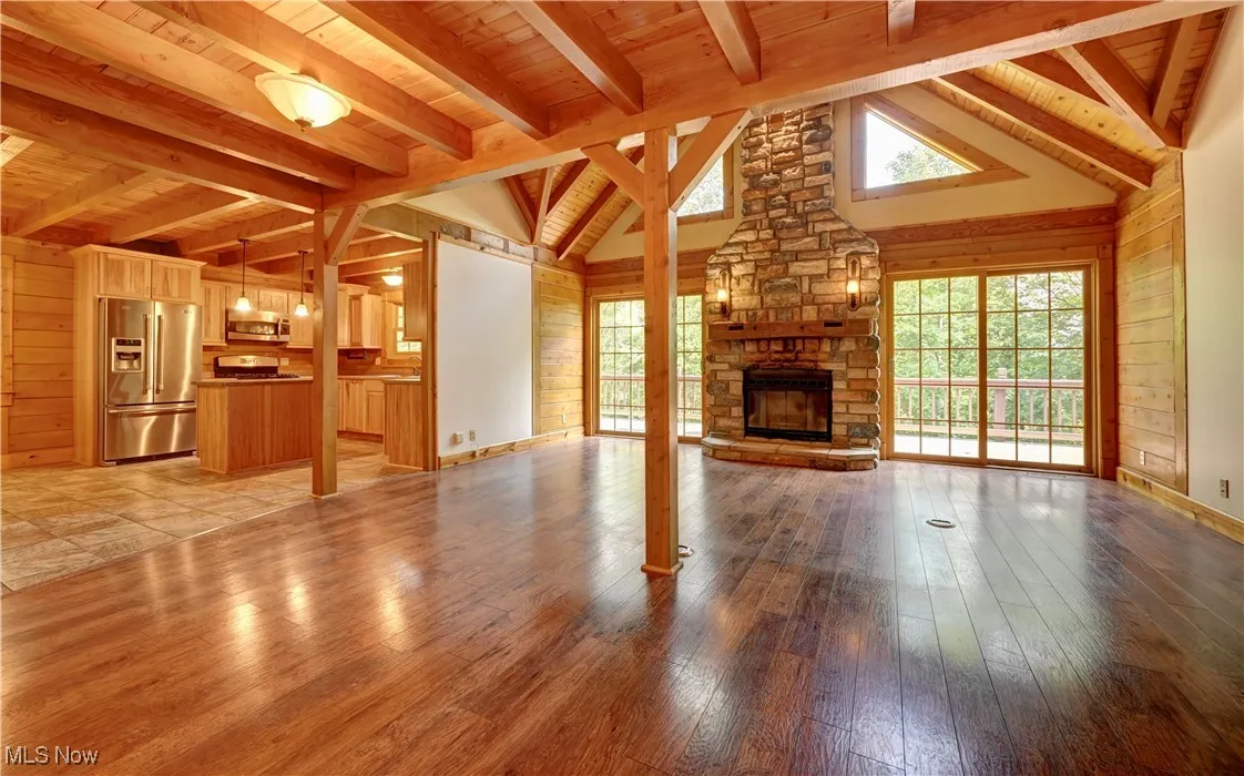 Unfurnished living room featuring wooden ceiling, light wood-style flooring, a stone fireplace, and wooden walls