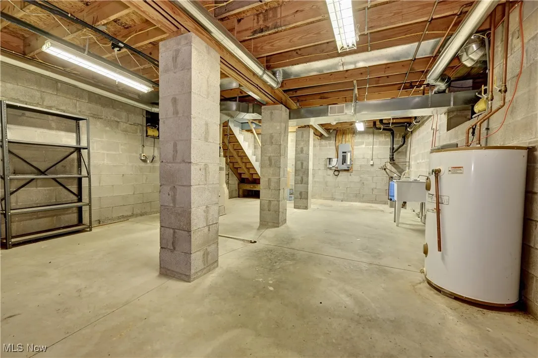 Unfinished below grade area with water heater, electric panel, and stairway