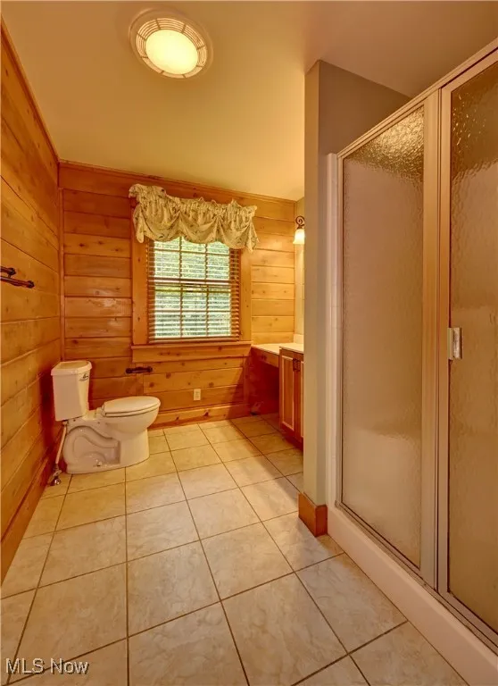 Bathroom with a stall shower, tile patterned floors, wood walls, and vanity