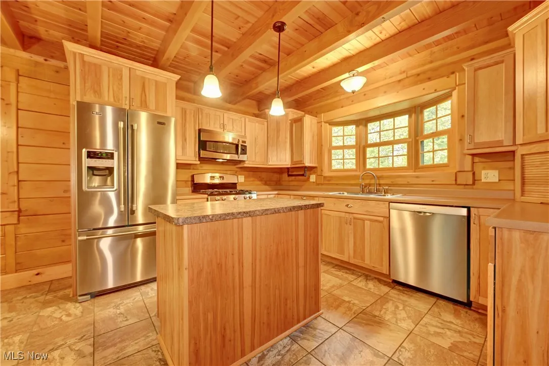Kitchen featuring stainless steel appliances, light brown cabinets, a wooden ceiling with exposed beams, light countertops, and a center island