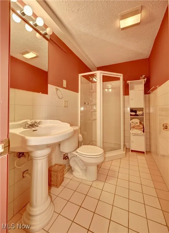 Bathroom featuring tile walls, a textured ceiling, a shower stall, tile patterned floors, and wainscoting