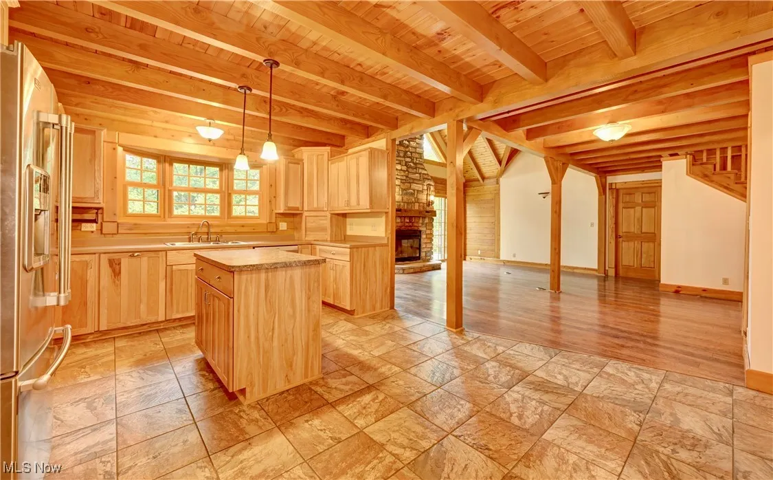 Kitchen featuring light brown cabinets, a wooden ceiling with exposed beams, a center island, light countertops, and stainless steel fridge