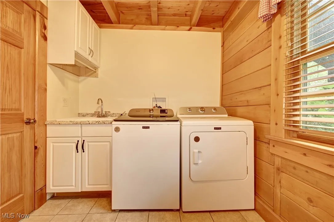 Washroom featuring cabinet space, washing machine and dryer, wood ceiling, light tile patterned floors, and wood walls