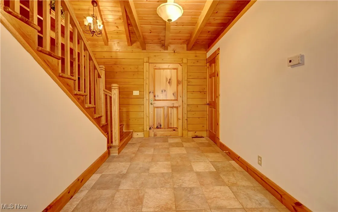 Hall featuring a wooden ceiling with exposed beams, stairway, wooden walls, and a chandelier