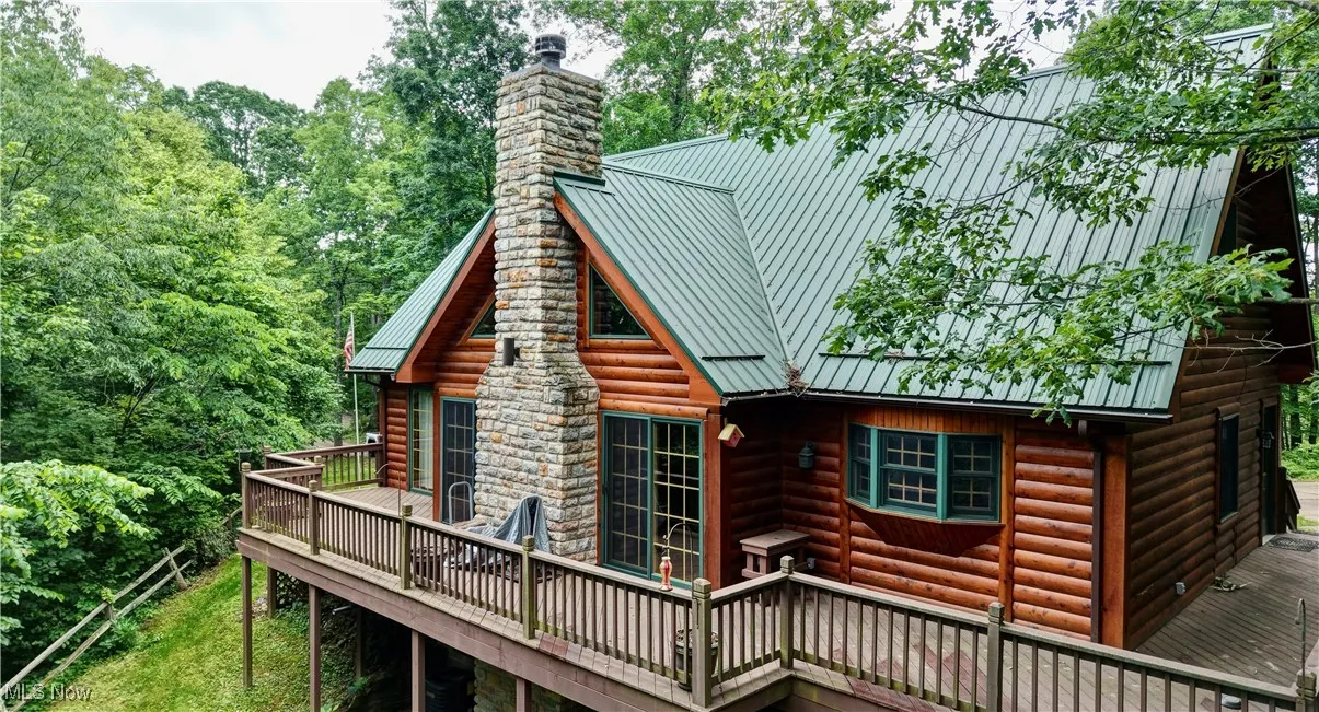 Back of property featuring a wooden deck, a chimney, faux log siding, and a metal roof