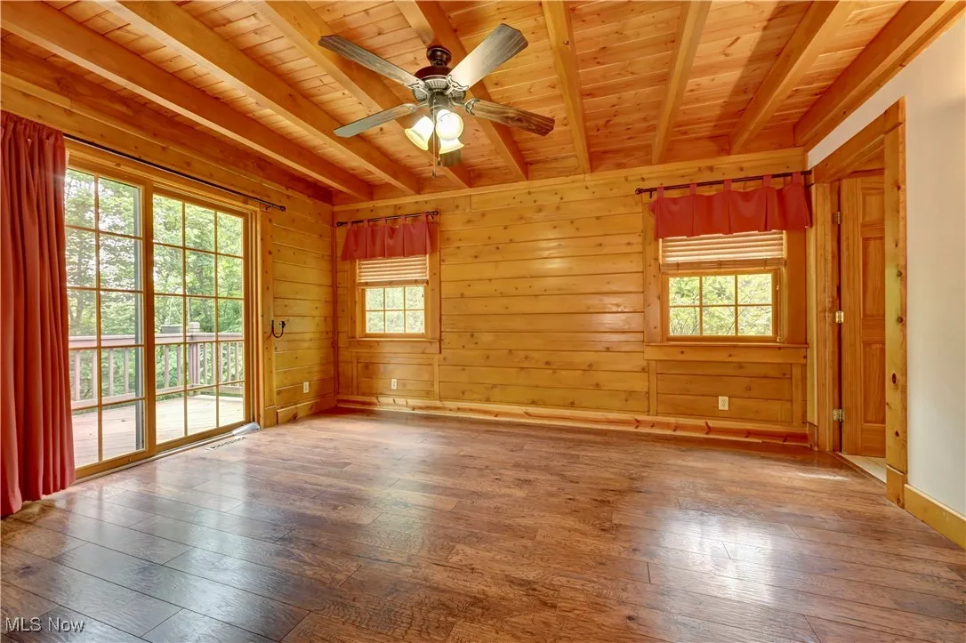 Unfurnished room featuring a wood ceiling with exposed beams, hardwood / wood-style flooring, ceiling fan, and wooden walls