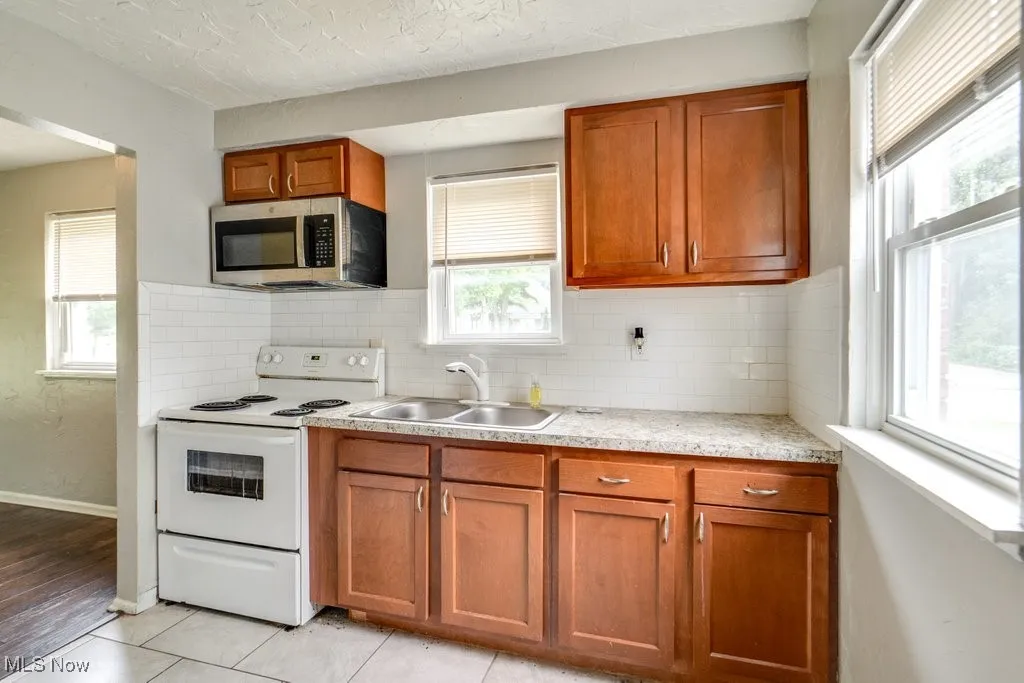 Kitchen featuring stainless steel microwave, white range with electric stovetop, light countertops, healthy amount of natural light, and a textured ceiling
