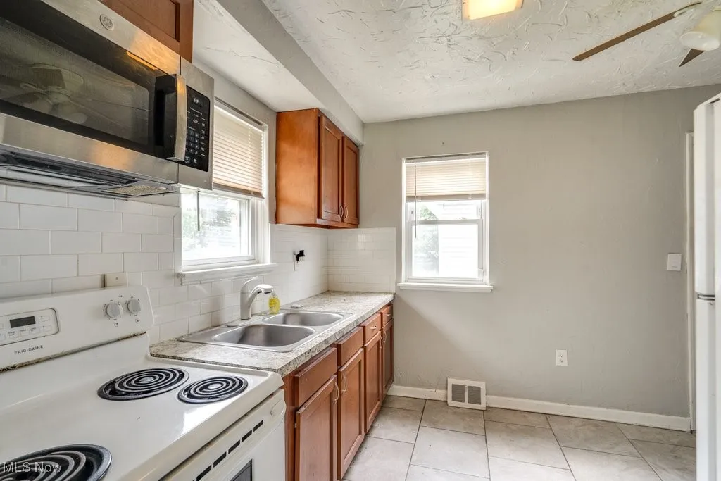 Kitchen featuring electric range, stainless steel microwave, healthy amount of natural light, brown cabinetry, and a textured ceiling