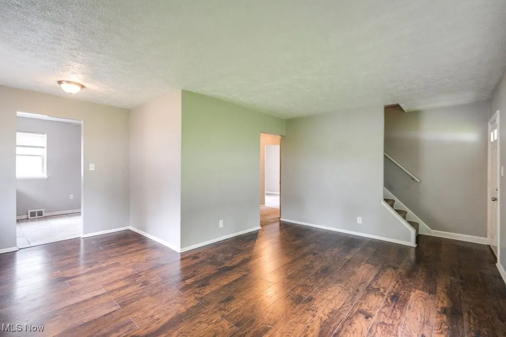Spare room with a textured ceiling, wood finished floors, and stairway