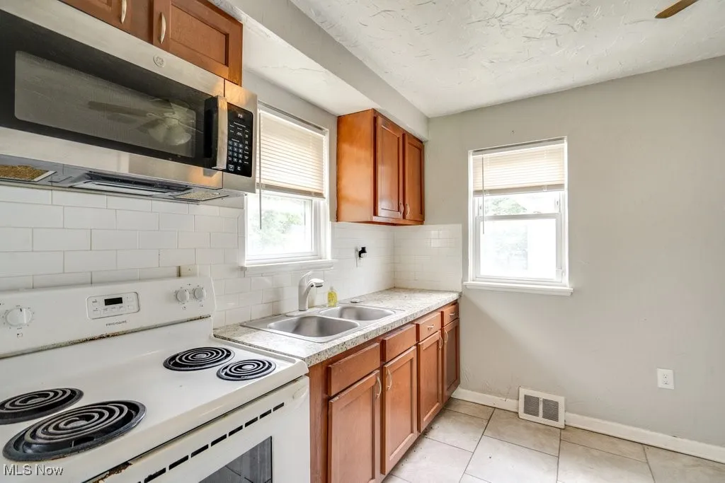 Kitchen featuring electric stove, stainless steel microwave, light countertops, tasteful backsplash, and brown cabinetry