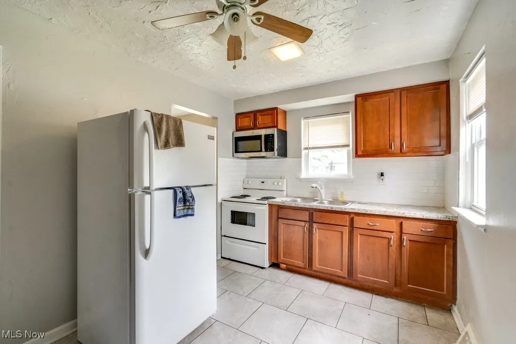 Kitchen featuring white appliances, light countertops, ceiling fan, tasteful backsplash, and brown cabinetry