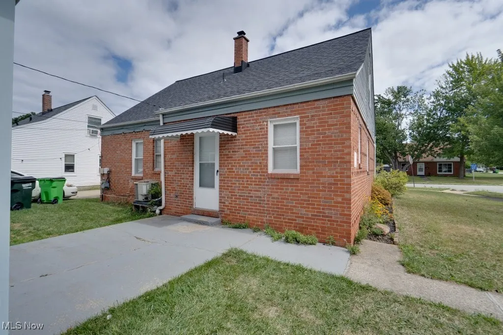 Rear view of house with a yard, a shingled roof, brick siding, and a chimney