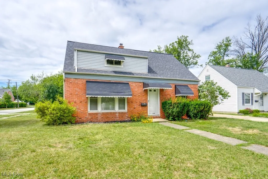 View of front facade featuring brick siding, a chimney, roof with shingles, and a front yard