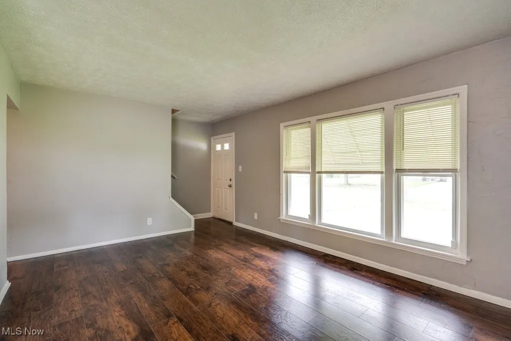 Unfurnished living room featuring dark wood-style flooring, stairway, and a textured ceiling