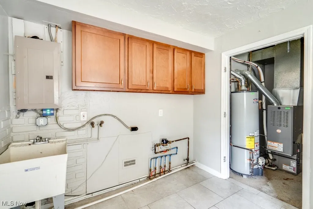 Laundry area featuring gas water heater, electric panel, cabinet space, and a textured ceiling