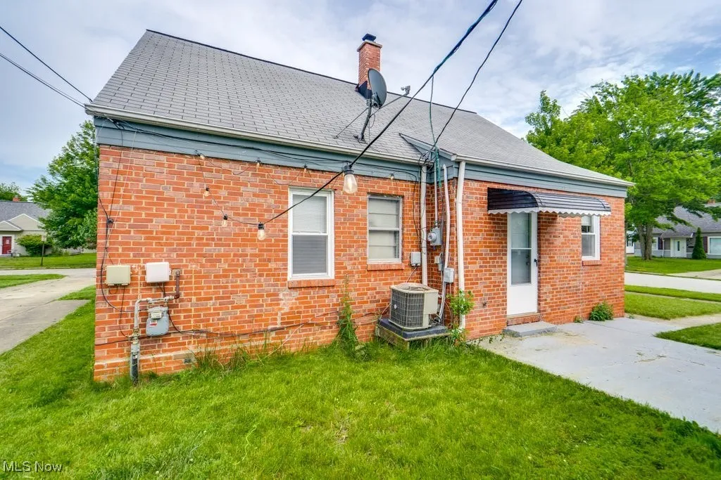 Rear view of property with brick siding, a yard, and a chimney