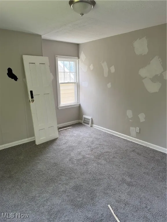 Spare room featuring dark carpet and a textured ceiling