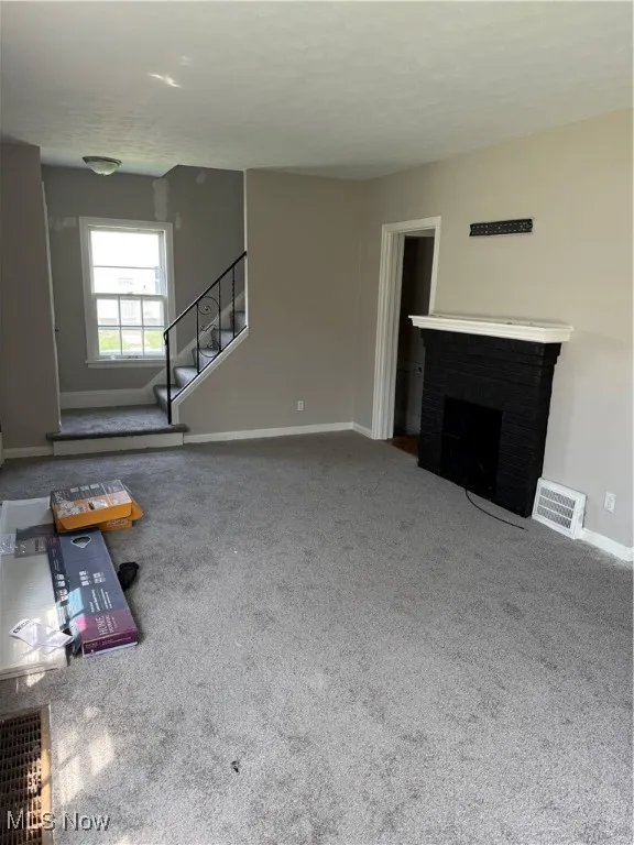 Unfurnished living room with carpet flooring, stairs, and a fireplace