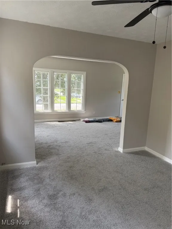 Unfurnished room featuring arched walkways, carpet flooring, a ceiling fan, and a textured ceiling