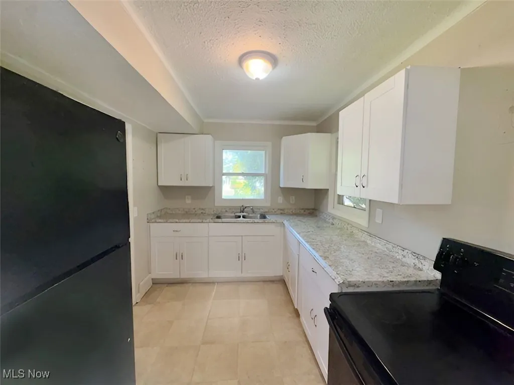 Kitchen with black appliances, a textured ceiling, white cabinets, and light stone counters