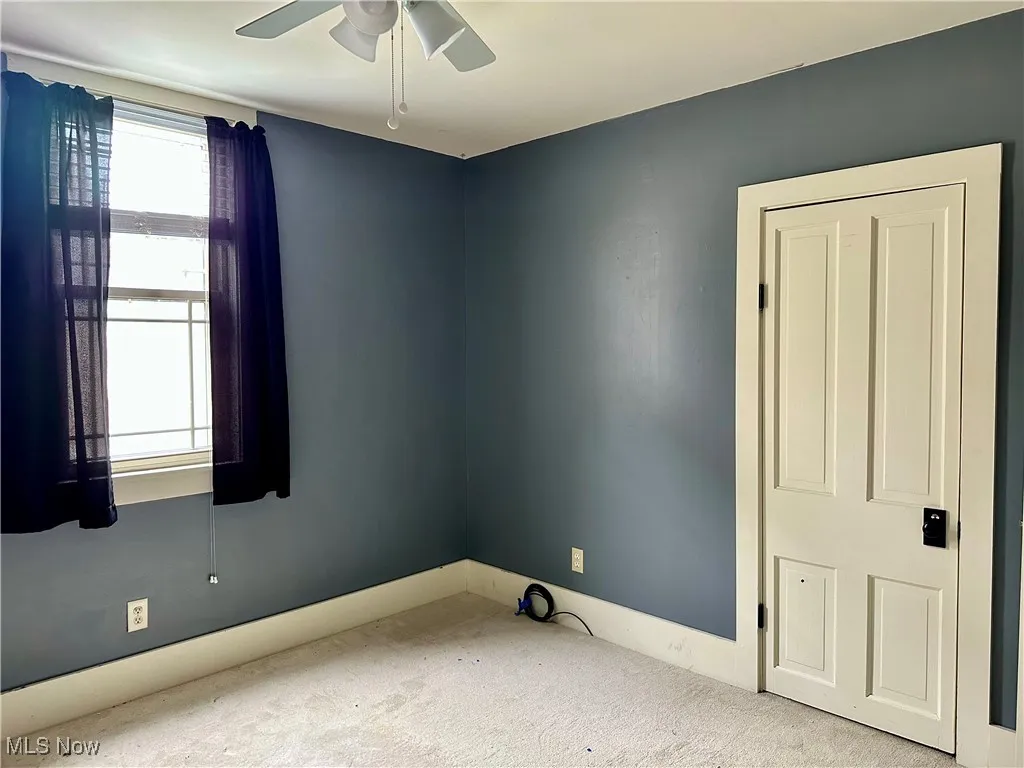 Carpeted spare room featuring ceiling fan and baseboards
