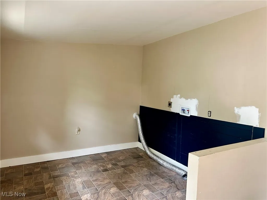 Laundry area with hookup for an electric dryer, hookup for a washing machine, and stone finish flooring