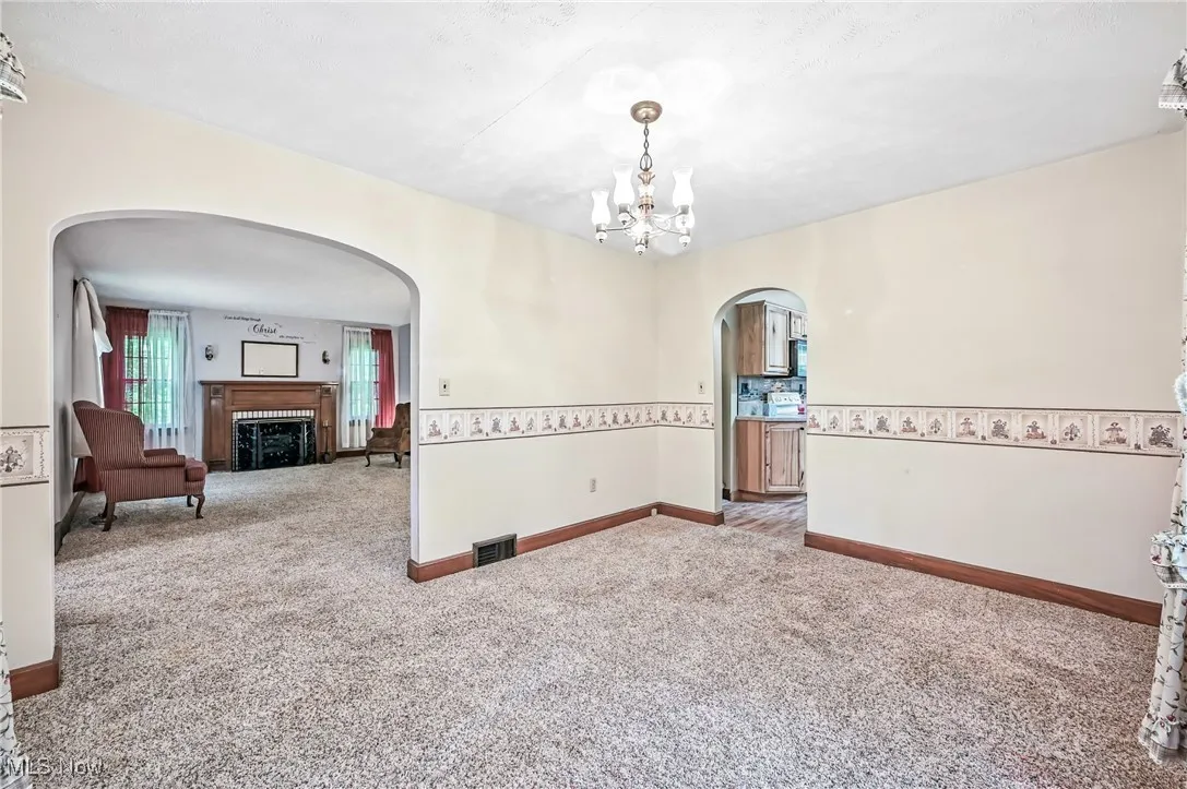Carpeted empty room with arched walkways, a chandelier, and a fireplace