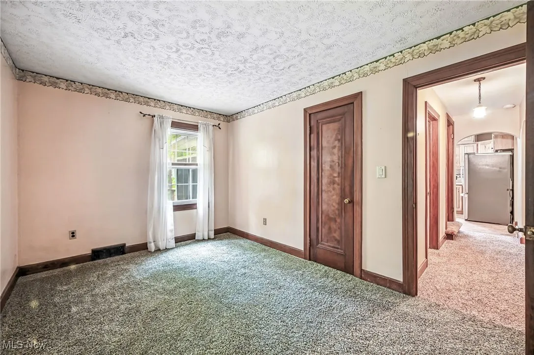 Carpeted empty room featuring arched walkways and a textured ceiling