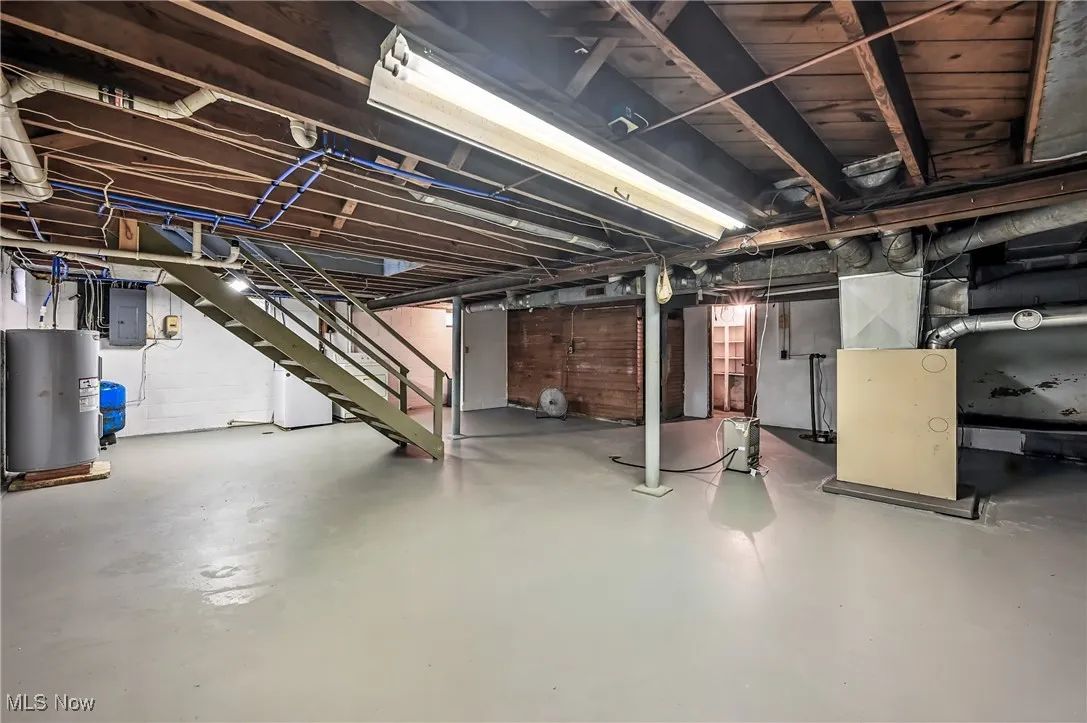 Unfinished below grade area with electric panel, electric water heater, and stairway