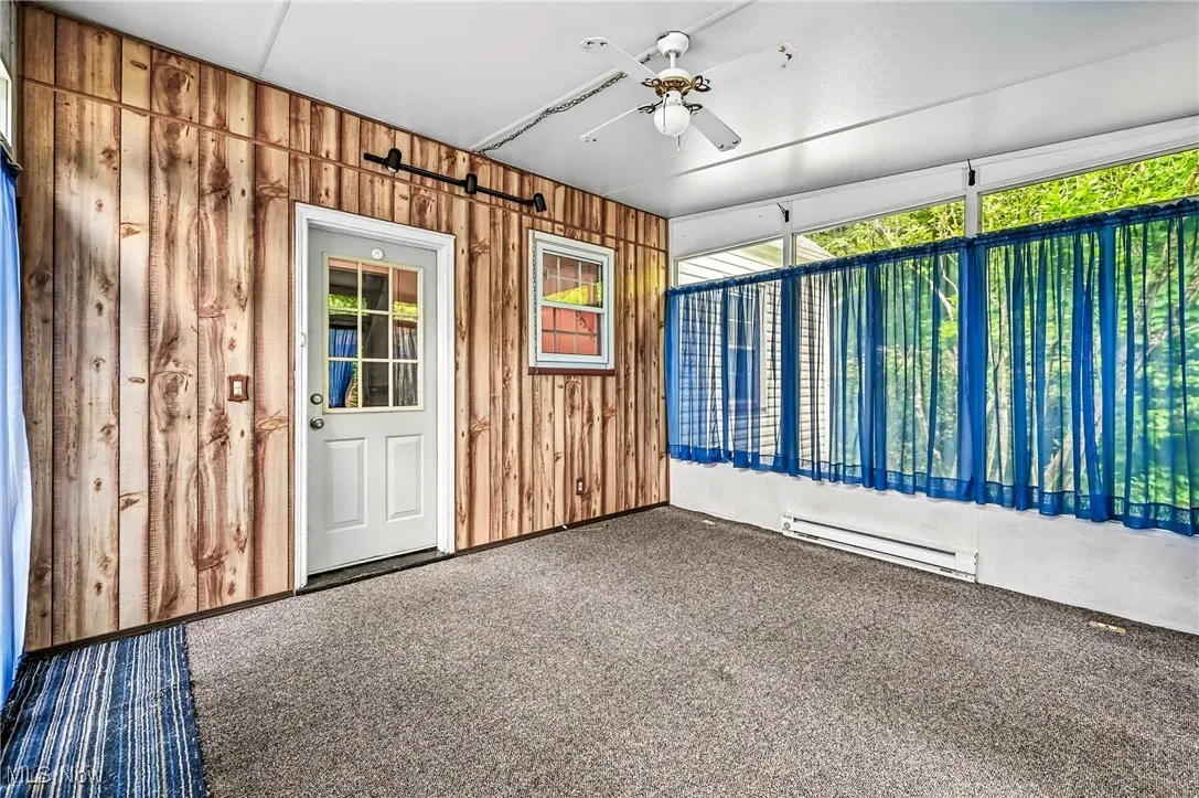 Carpeted empty room with baseboard heating, ceiling fan, and wood walls