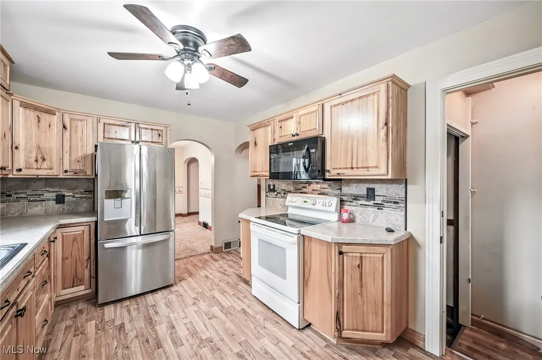 Kitchen with stainless steel refrigerator with ice dispenser, black microwave, white electric range, arched walkways, and backsplash