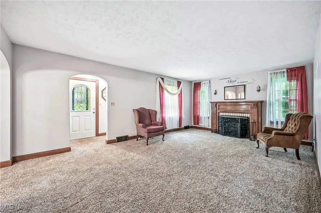 Living area with arched walkways, carpet floors, plenty of natural light, a textured ceiling, and a fireplace