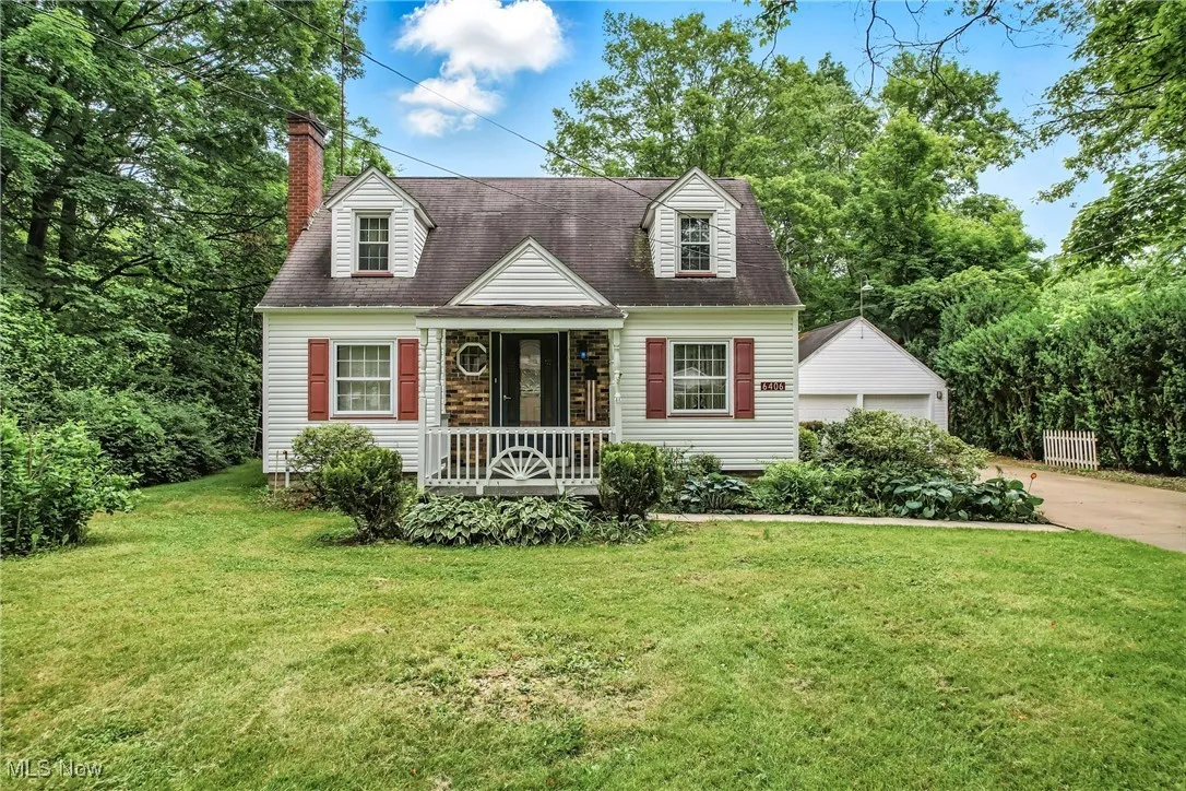 Cape cod home with a porch, a front lawn, a chimney, and a garage