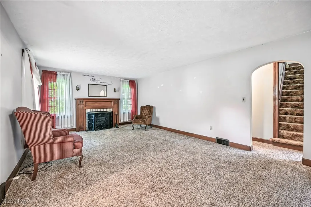 Carpeted living room featuring a fireplace, arched walkways, stairway, and a textured ceiling