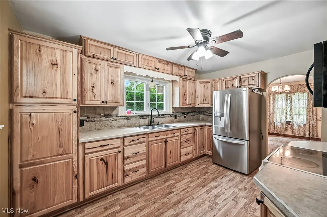 Kitchen featuring stainless steel refrigerator with ice dispenser, black microwave, backsplash, ceiling fan, and light countertops
