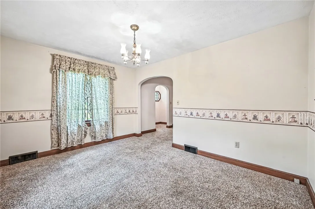 Carpeted spare room featuring arched walkways and a chandelier