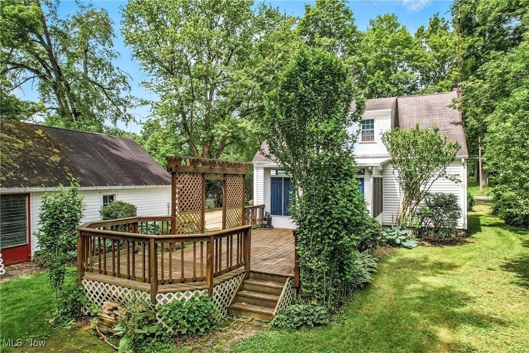 Back of house featuring a wooden deck, a pergola, a lawn, and a shingled roof