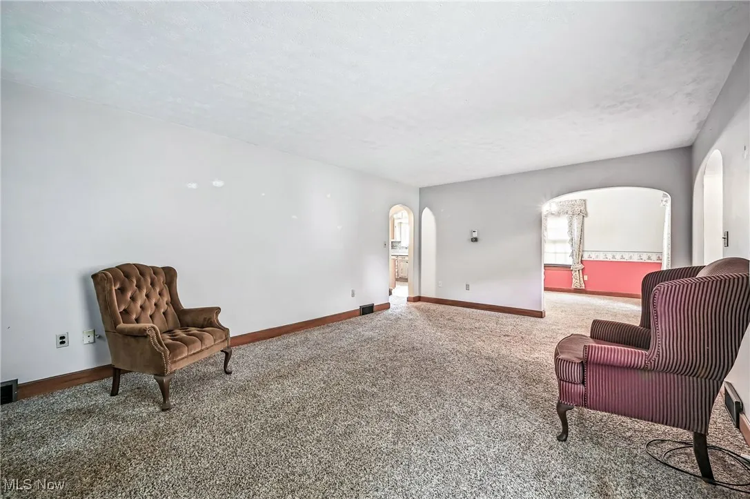 Living area featuring arched walkways, carpet, and a textured ceiling