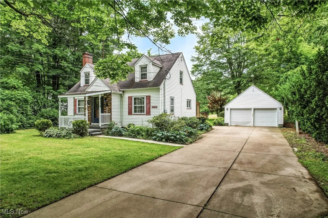 Cape cod-style house featuring a porch, an outdoor structure, a detached garage, and a front lawn