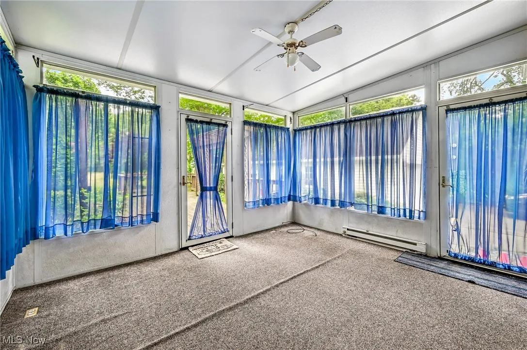 Unfurnished sunroom with a baseboard radiator, plenty of natural light, carpet, and vaulted ceiling
