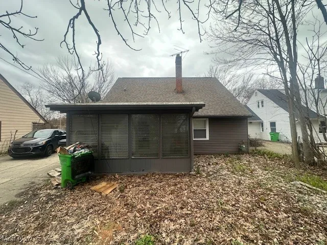 Back of house with a sunroom, a chimney, and roof with shingles