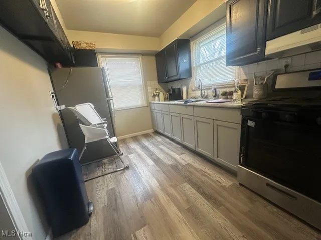 Kitchen with stainless steel gas range oven, light wood-type flooring, tasteful backsplash, light countertops, and under cabinet range hood