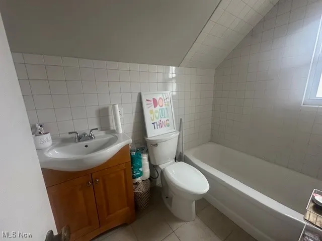 Full bathroom featuring tile patterned floors, vanity, tile walls, and vaulted ceiling