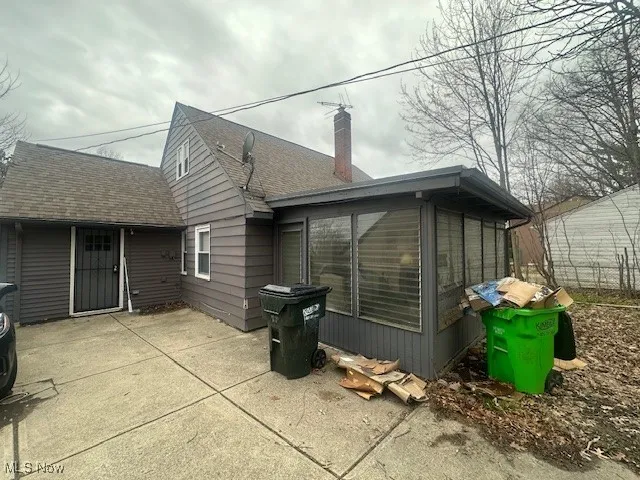 Back of house with a sunroom, a chimney, roof with shingles, and a patio area