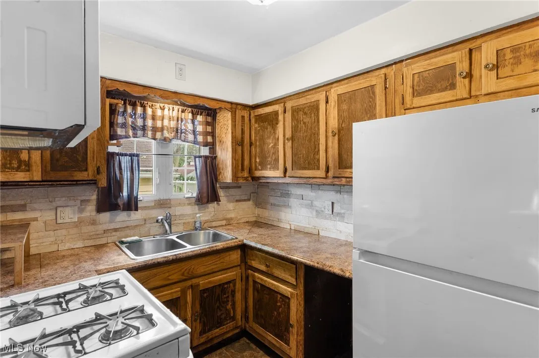 Kitchen featuring white appliances, tasteful backsplash, light countertops, and brown cabinetry