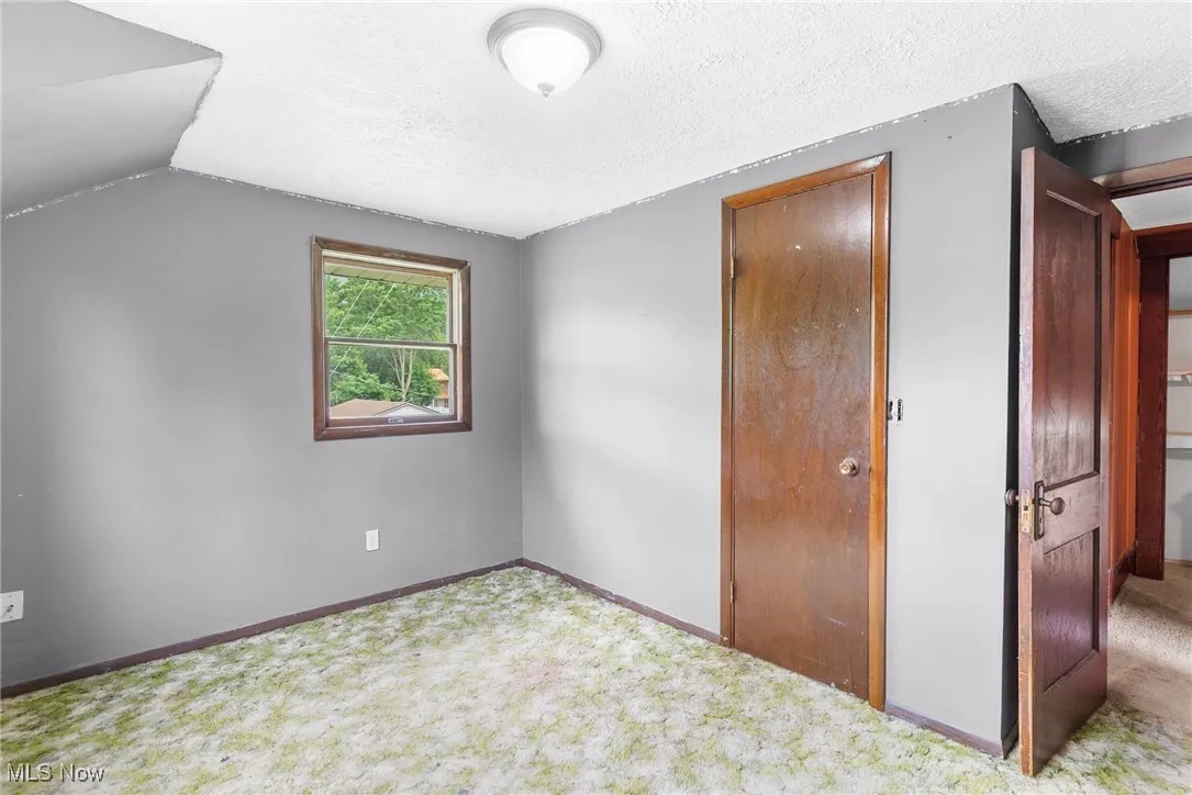 Unfurnished bedroom with carpet, a textured ceiling, and vaulted ceiling